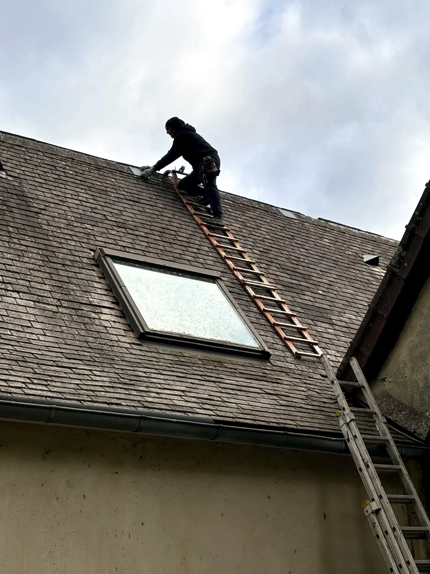 Couvreur sur une échelle de toit posée sur un versant d'ardoise