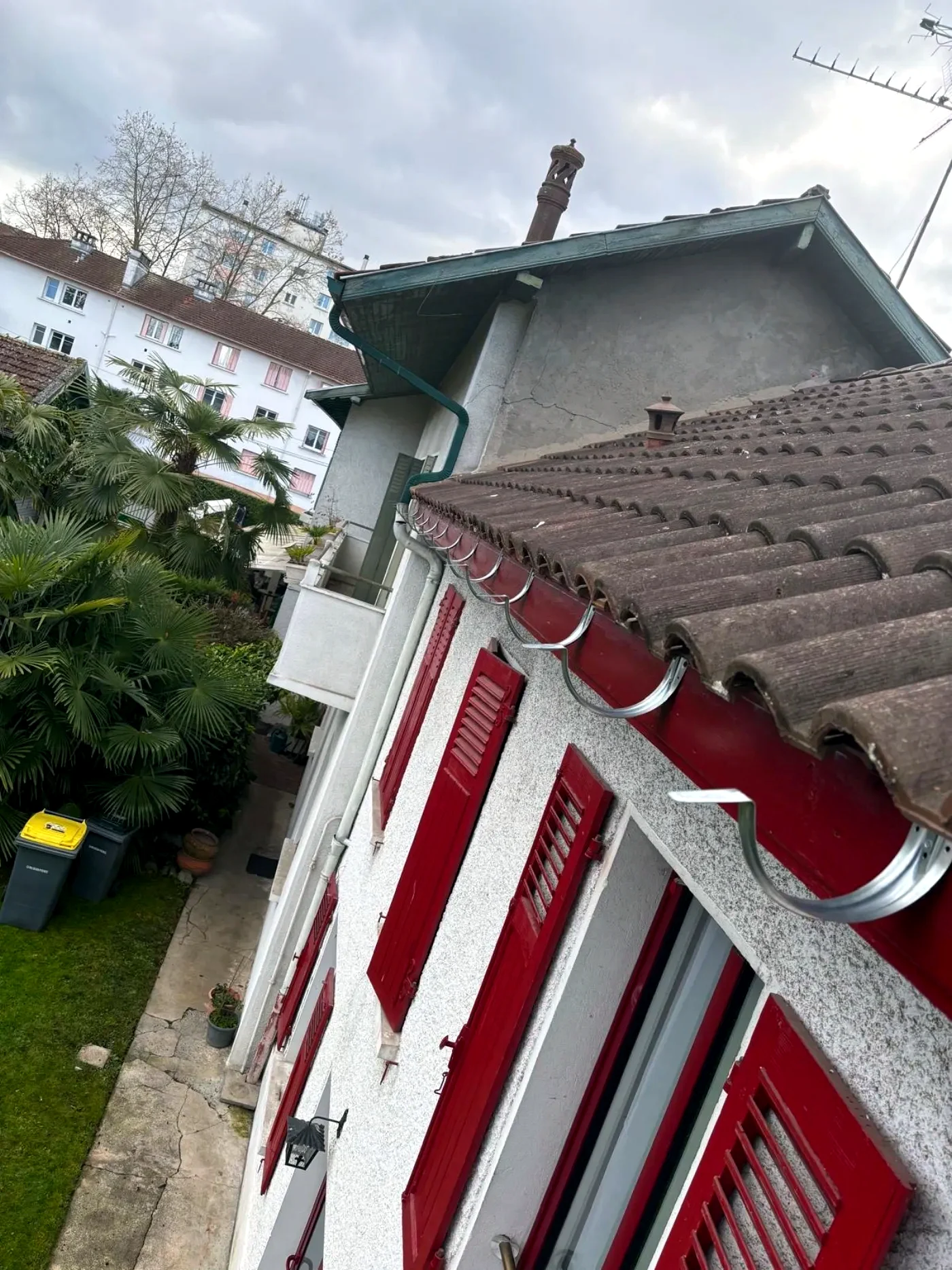 Gouttière et descente le long d'une façade à volets rouges